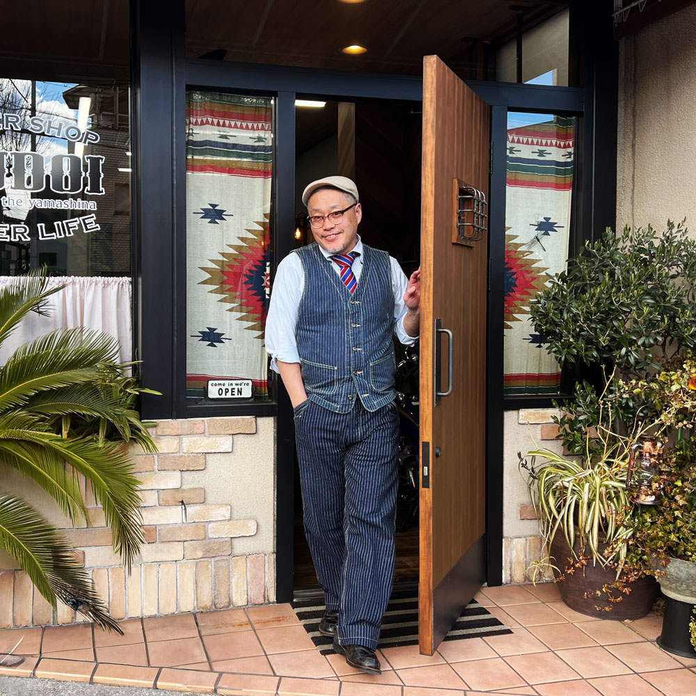 WOOD DEPOTの木製ドアの前で笑顔を見せるマスター