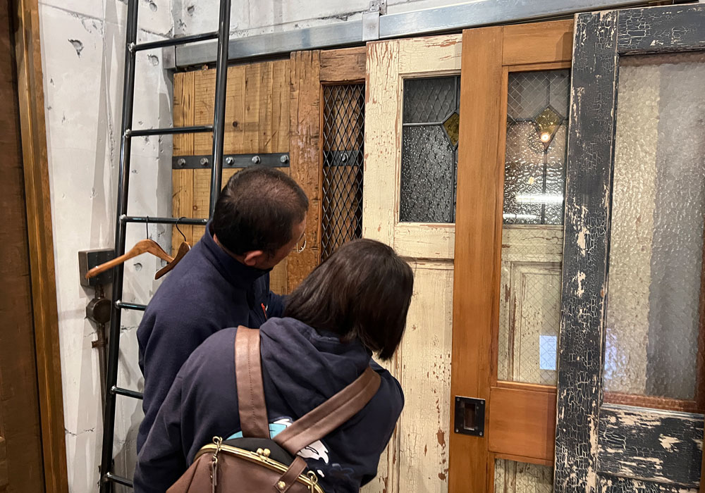 「オーガニックカフェの顔」を選ぶ富山のご夫婦：ショールームでの木製ドア選び風景