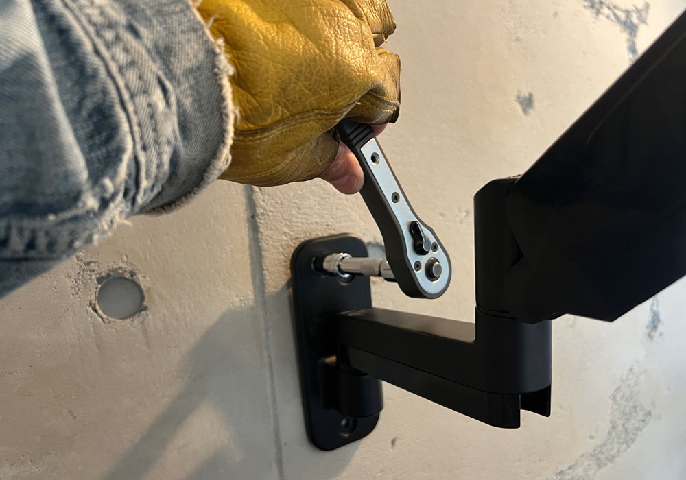 コンクリート壁にモニターアームを固定する作業風景