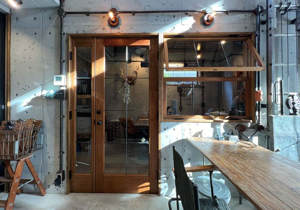 WOOD DEPOTショールームに見る、カフェデザインの実例 打ちっ放しのコンクリートに映えるあたたかい陽の光を浴びた木製室内ドアと室内窓