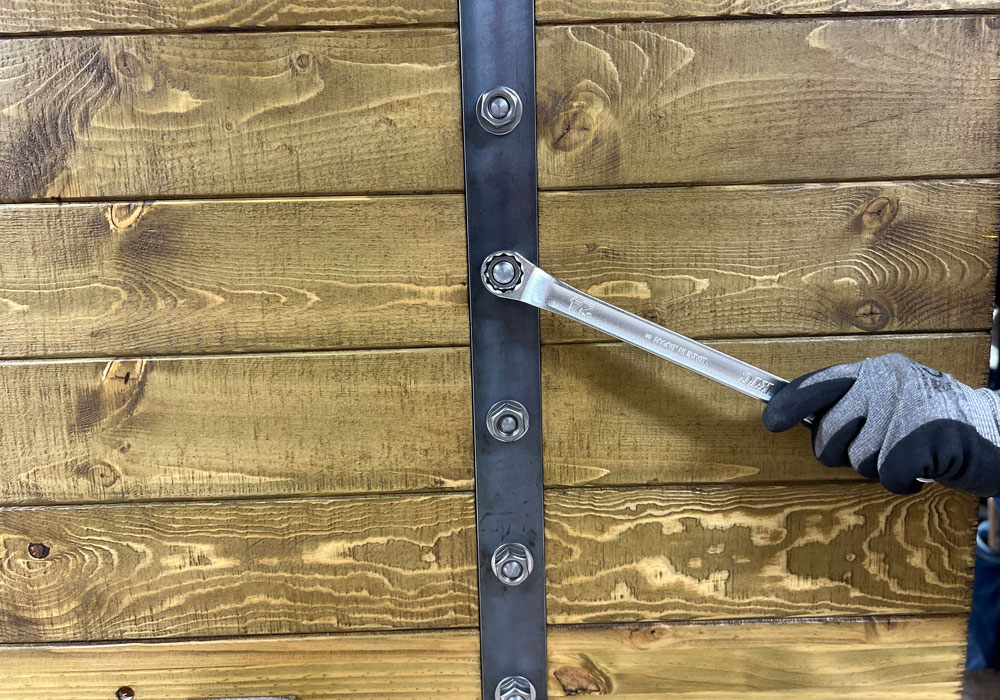 職人が木製ドアの鉄ボルトを手作業で締め付けている様子